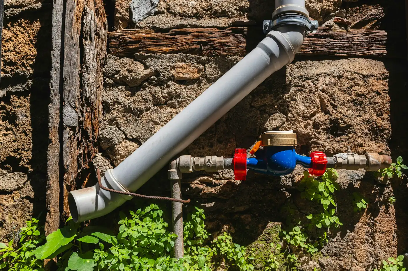 Blue residential water meter on a grey supply pipe against a stone wall