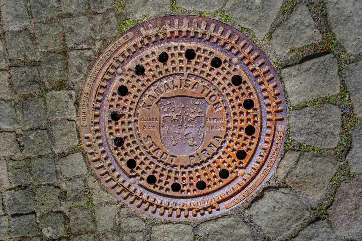 Rusty cast-iron sewer manhole cover set in stone pavement