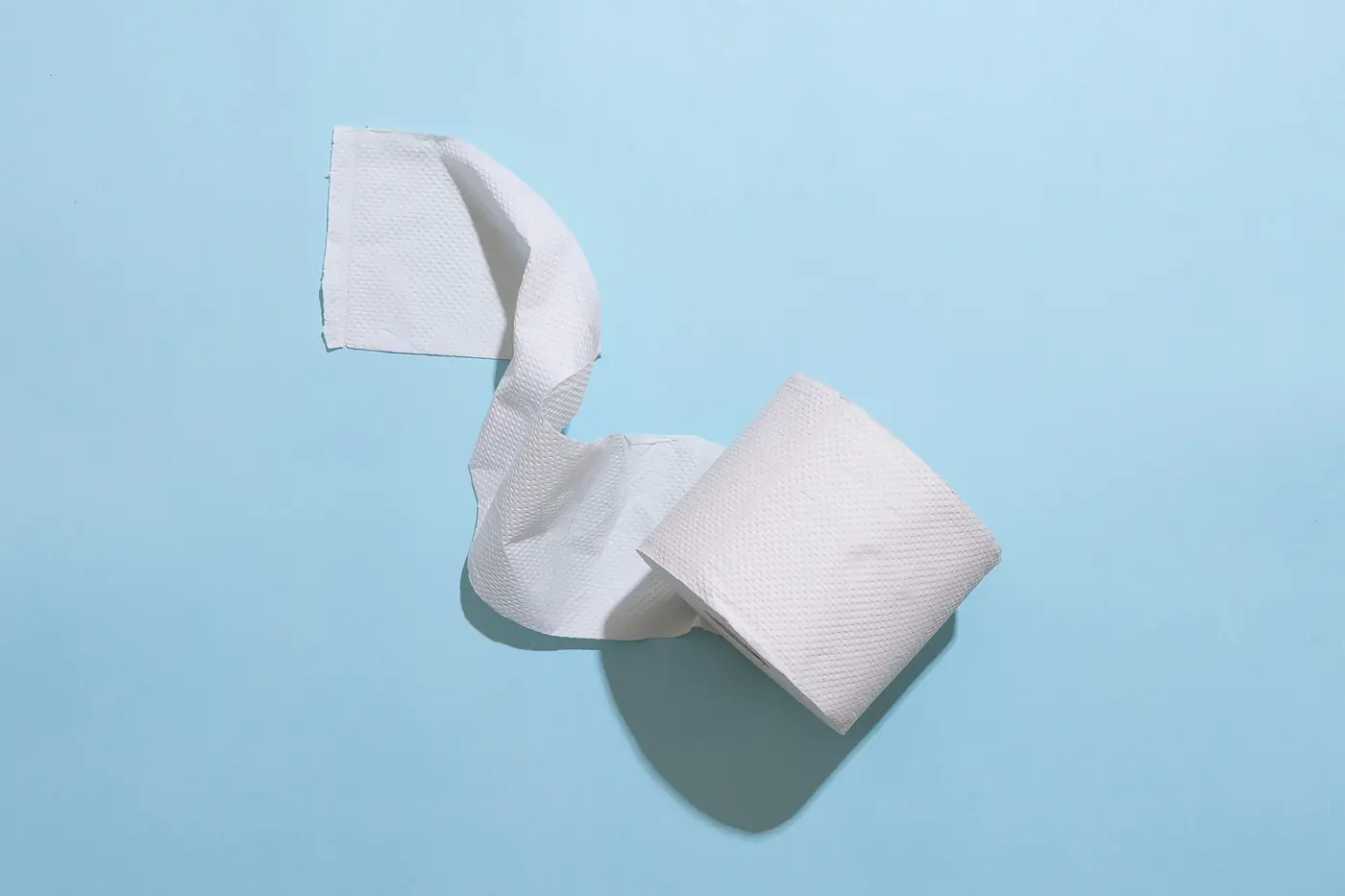 Roll of toilet paper partly unrolled on a light blue background