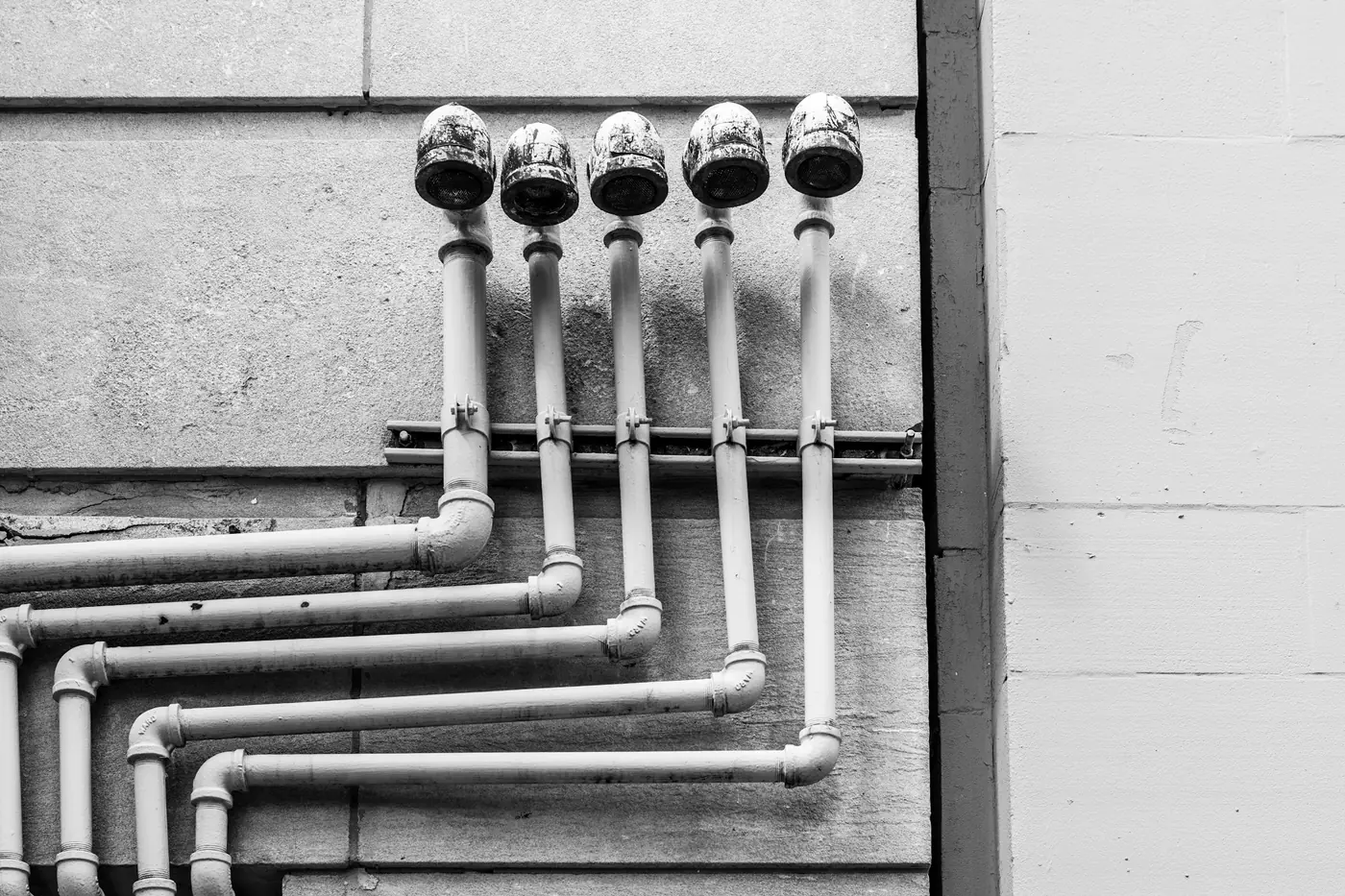 Black and white photo of white pipes with valves mounted on a wall